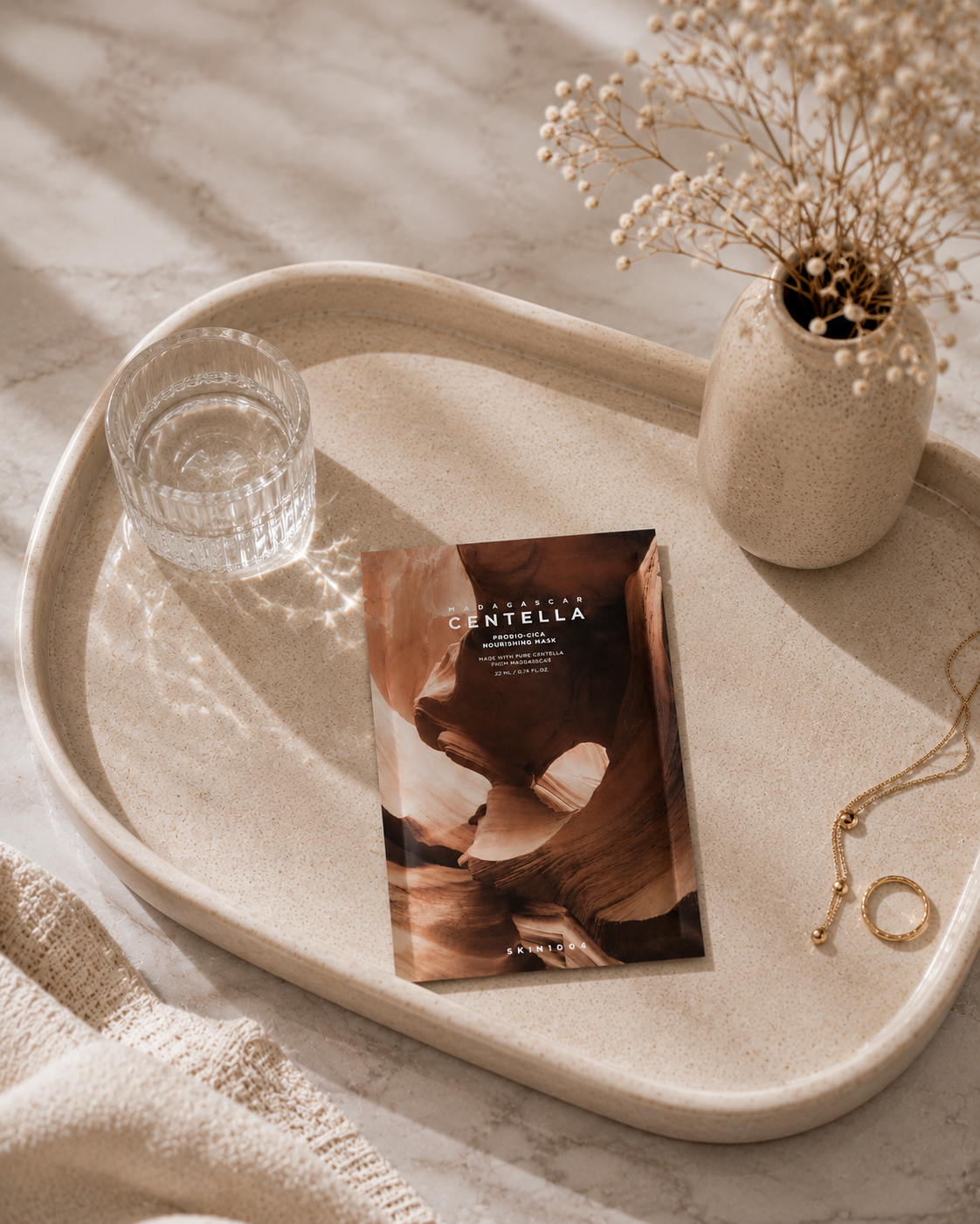 Tray with Skin1004 Madagascar Centella Probio-Cica Nourishing Mask 22ml x 5ea, glass, vase with dried flowers, and necklace.